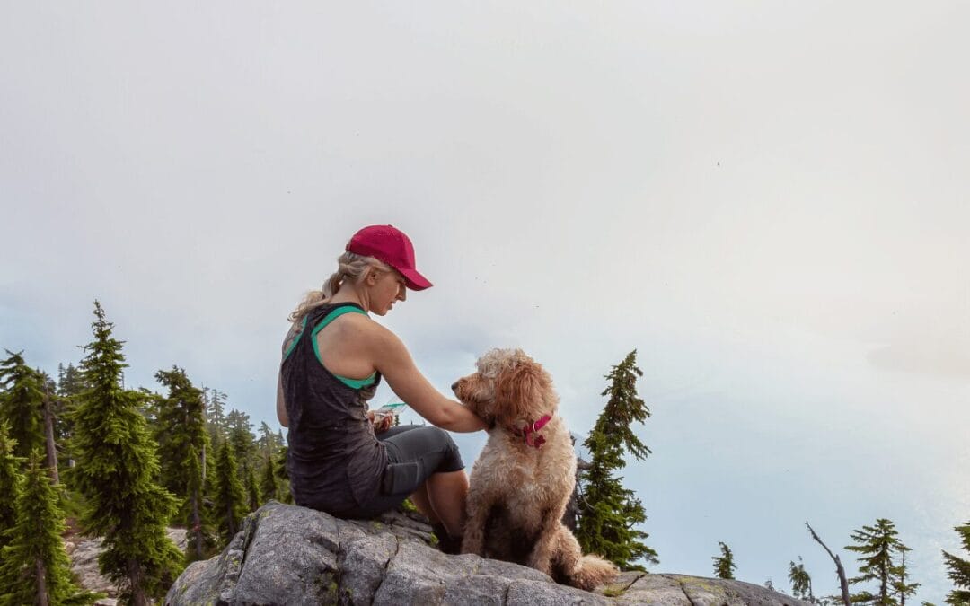 Mujer con gorra roja haciendo senderismo con su perro en la cima de una montaña rodeada de pinos, actividad pet friendly cerca de la CDMX.